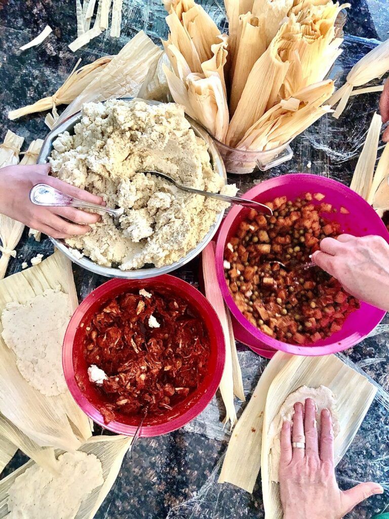 Hands preparing antojitos from bowls of fillings and red salsa