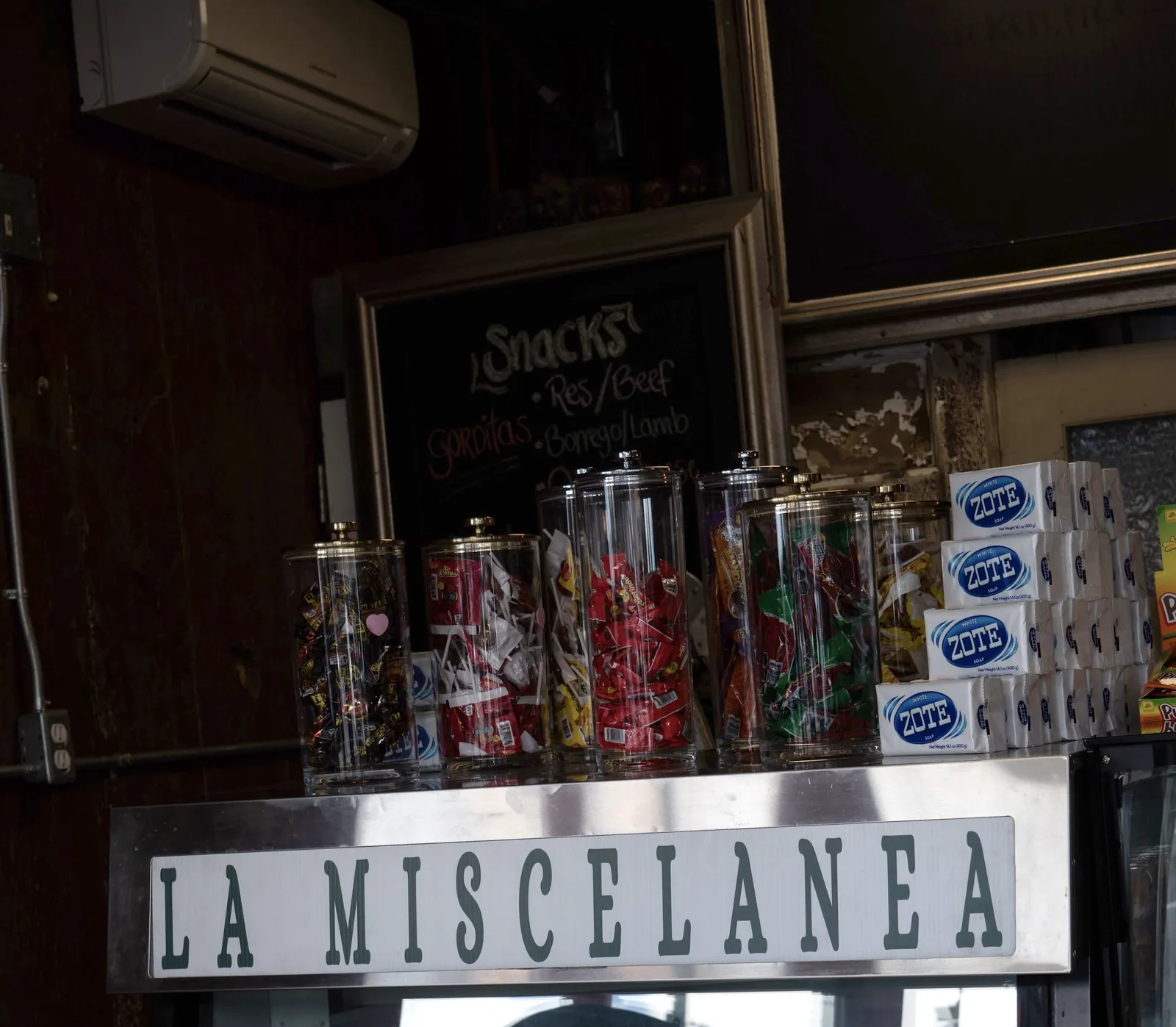 The La Miscelánea counter sign beneath jars of Mexican candy, stacked Zote soap and a chalkboard snack menu