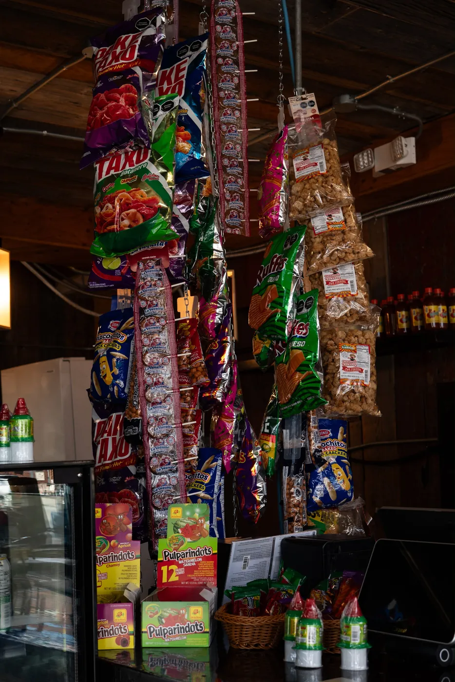 Strings of Mexican chips and candies hanging over the counter — Takis, Ruffles, La Vaquita lollipops, chicharrón and Pulparindots